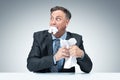 Frightened businessman in a dark jacket, shirt and tie eats paper on light grey background. The concept of document destruction