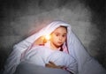 Frightened girl with flashlight under blanket