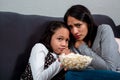 Frightened girls sisters sitting on the sofa looking at the camera. Watching tv horror film together with popcorn Royalty Free Stock Photo