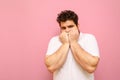 Frightened guy in a white T-shirt and curly overweight hair, looks into the camera and covers his face with his hand in fear.