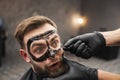 Frightened man grimaces while removing black facail skin mask in beauty salon. Royalty Free Stock Photo