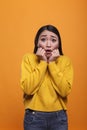 Frightened scared young adult woman covering mouth with hands in fear on orange background.