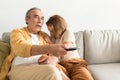 Frightened senior european spouses watching TV, man holding remote control and woman closing face, sitting on sofa Royalty Free Stock Photo