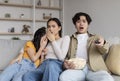 Frightened shocked asian millennial wife, husband and adolescent daughter watching scary movie and eating popcorn