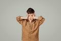 Frightened shocked little child 6 years old in shirt presses his hands to head on gray studio background