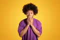 Frightened shocked mature black curly man in purple t-shirt covers his mouth with hands