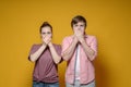 Frightened woman and a man in casual clothes cover their mouths with their hands and stare in shock, on a yellow Royalty Free Stock Photo