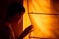 Frightened young man stands beside window