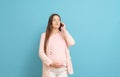 Frightened young pregnant woman on blue background calls by mobile phone, discharge of amniotic fluid, the beginning of labor