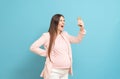 Frightened young pregnant woman on blue background calls by mobile phone, discharge of amniotic fluid, the beginning of labor