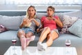 Frightened young women watching scary movie at home. Girls watching a terror horror movie on tv sitting on a couch at home. Scary Royalty Free Stock Photo