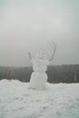 Frightening snowman with hands made of branches during a snowfall on a forest background. Snow sculpture with ominous look