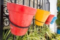 Arrangement of four vibrant pails suspended from a black gate in a pastoral setting