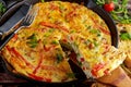 Frittata made of eggs, potato, bacon, paprika, parsley, green peas, onion, cheese in iron pan. on wooden table.