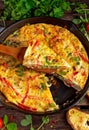 Frittata made of eggs, potato, bacon, paprika, parsley, green peas, onion, cheese in iron pan. on wooden table.