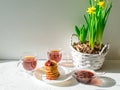 Fritters with strawberry jam, two cups of tea and a bouquet of yellow daffodils in a basket on a white background. Royalty Free Stock Photo