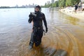 Frogman standing in water and showing a crab, beach and beachgoers on a background