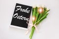 Frohe Ostern means Happy Easter text on black chalkboard with tulip flower on white background,floral spring decorations