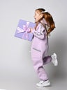 Frolic laughing kid girl in pink jumpsuit is running holding big blue gift box, birthday present in hands. Side view Royalty Free Stock Photo
