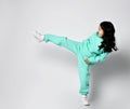 Frolic asian kid girl in pastel green, mint color hoodie and pants stands sideways playing fighter, kicking Royalty Free Stock Photo
