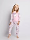 Smiling blonde kid girl in stylish shirt and pants pyjamas with flower print pattern stands holding hand at her leg