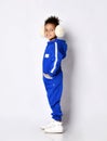 Frolic dark-skinned kid girl in warm blue trendy jumpsuit and white sneakers stands looking back. Side view