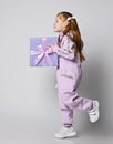 Frolic smiling kid girl in pink jumpsuit is running with big blue gift box with ribbon and bow in hands. Side view