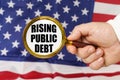 In front of the American flag, a man holds a magnifying glass in his hand with the inscription - rising public debt