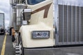 Front of the beige classic bonnet big rig semi truck tractor with semi trailer standing on the truck stop parking lot