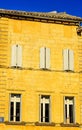 front of yellow, lime, block building, with three pair of sutteres, covering three window and three window with open shutters