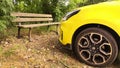 Front of a bright yellow car parked near an old wooden bench