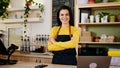 In front of the camera posing barista woman with a perfect large smile and crossing hands in a modern coffee shop