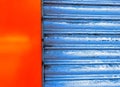 Front closeup of closed blue metal rolling shutter of a shop along with freshly painted red-orange wall Royalty Free Stock Photo