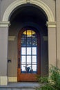 Front door entranceway with glass door and cement stucco archway with plants and visible lighting overhead in daylight