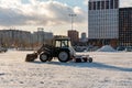 A front-end wheel loader clears the area from snow after a snowfall against the backdrop of residential buildings on a sunny day