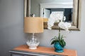 Front entryway table decor of a lamp and orchid with a mirror and orange runner on a gray dresser table
