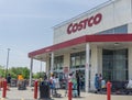 Front facade of Costco hypermarket building with face masked shoppers