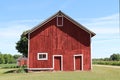 A front facing view of a wonderful old red barn with white trim and landscaped lawn with dirt road