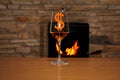 In front of the fireplace, in which firewood burns with a bright flame, there is one glass of wine, the dollar sign Royalty Free Stock Photo