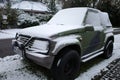 The front of a green snow covered Suzuki Vitara