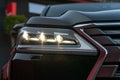 Front illuminated headlights of a black luxury modern car. Close up detail on one of the LED headlights with flare of
