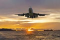 Front image commercial passenger aircraft or cargo airplane fly over coast of sea in evening with golden sunset seascape view and Royalty Free Stock Photo