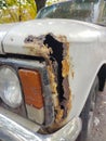 The front of an old car with a big hole from rust. You can see the headlight, bumper and wheel Royalty Free Stock Photo