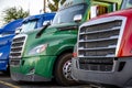 Front part of big rig semi trucks with chrome grilles and plastic bumpers standing in row on truck stop parking lot