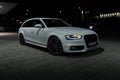 Front part of white Audi A4 Avant with lit headlights outdoors at night