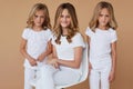 Front portrait of three sisters with blond hair dressed in white clothes, isolated beige background Royalty Free Stock Photo