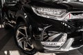 Front right modern headlight on luxury black new car in automobile salon. Detail metallic bumper car with LED headlights