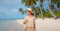 Front shot of brunette woman , dressed in safari look and a hat, walks on empty tropical beach Royalty Free Stock Photo