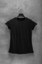 Front side of female black cotton t-shirt on a hanger and a concrete wall in the background Royalty Free Stock Photo