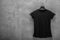 Front side of female black cotton t-shirt on a hanger and a concrete wall in the background Royalty Free Stock Photo